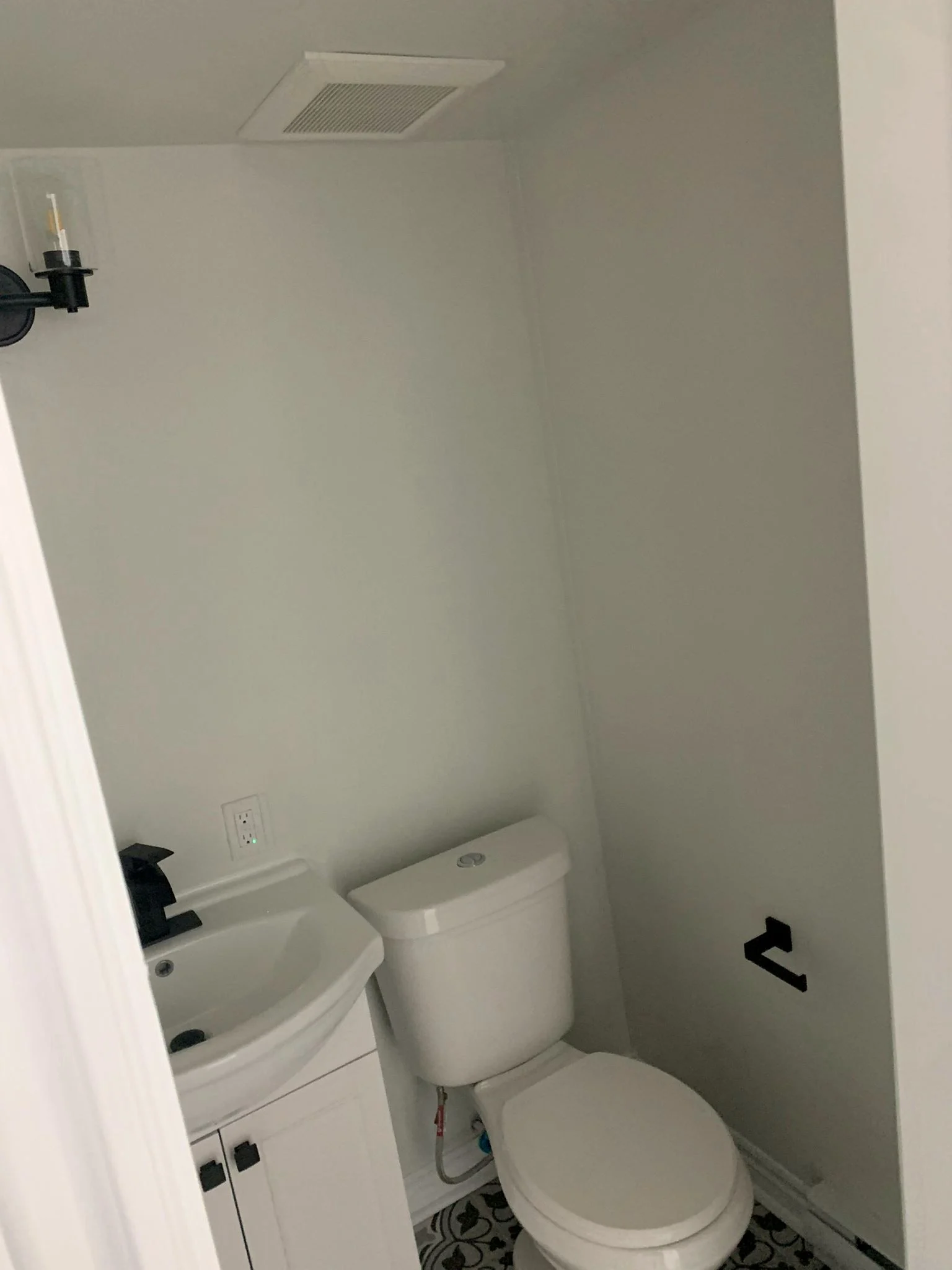 Finished powder room with a white toilet, a white vanity with a black faucet, and black and white patterned floor tile.
