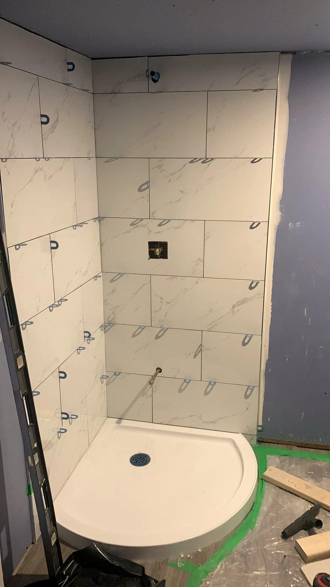 Corner shower with large format marble-look tile on leveling clips, a curved white shower base, and the mixing valve rough in still exposed.