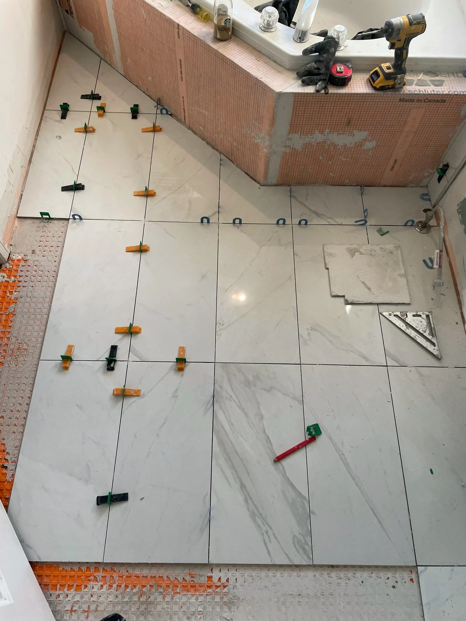 Floor tile being set on leveling clips beside the corner tub, with the tub apron wrapped in orange Kerdi board.