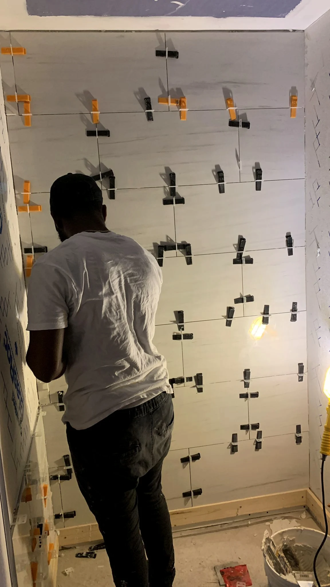 A member of the crew setting large-format wall tile, held in place with leveling clips across the finished courses.